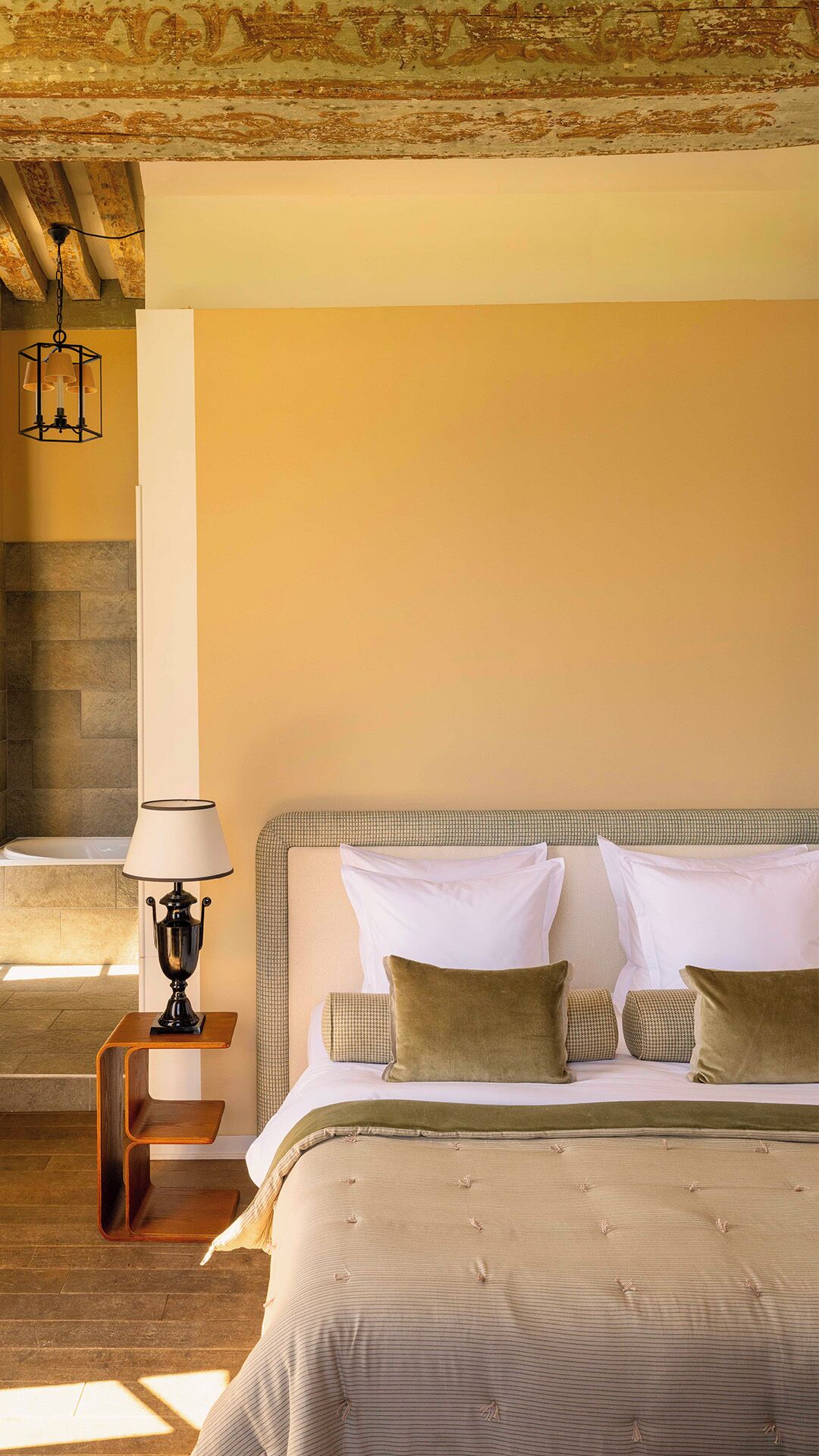 Un dormitorio con cama, almohadas, mesita de noche, lámpara y una escalera.