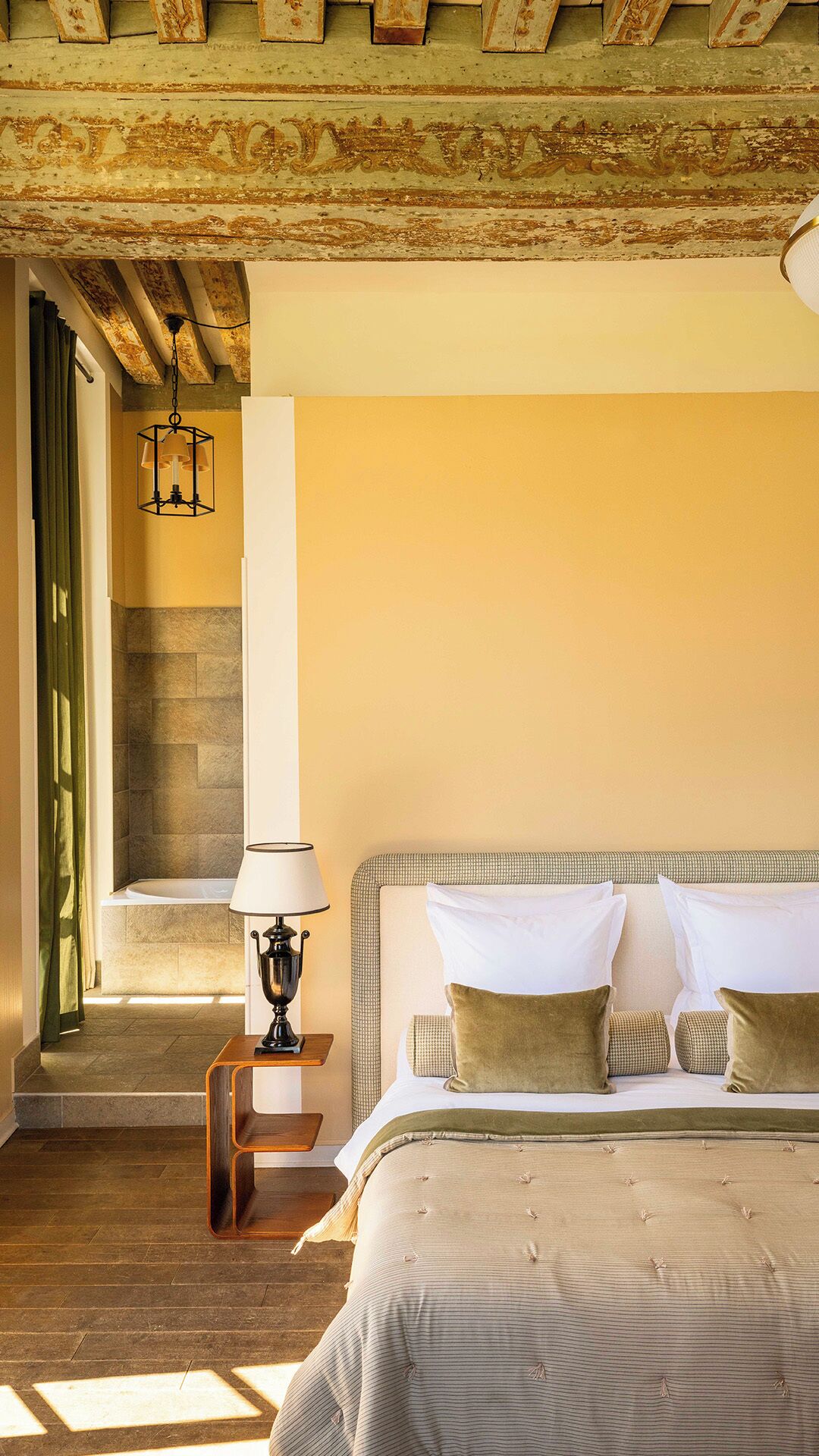 Un dormitorio con cama, mesita de noche, lámpara, pared de piedra y ventana.
