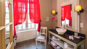 A bathroom with a white sink, red curtains, a hairdryer, and a chair.