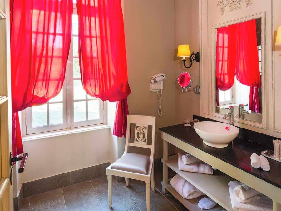 A bathroom with a white sink, red curtains, a hairdryer, and a chair.