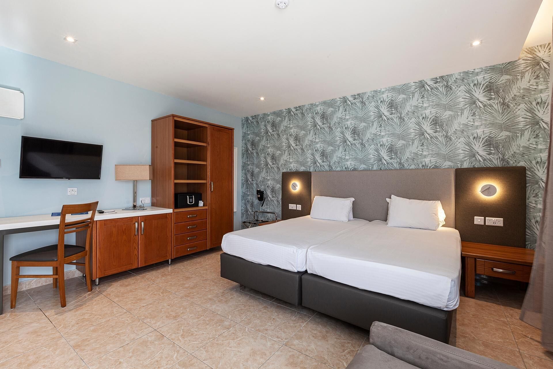 A hotel room with a bed, a desk, a chair, a wardrobe, and a television.