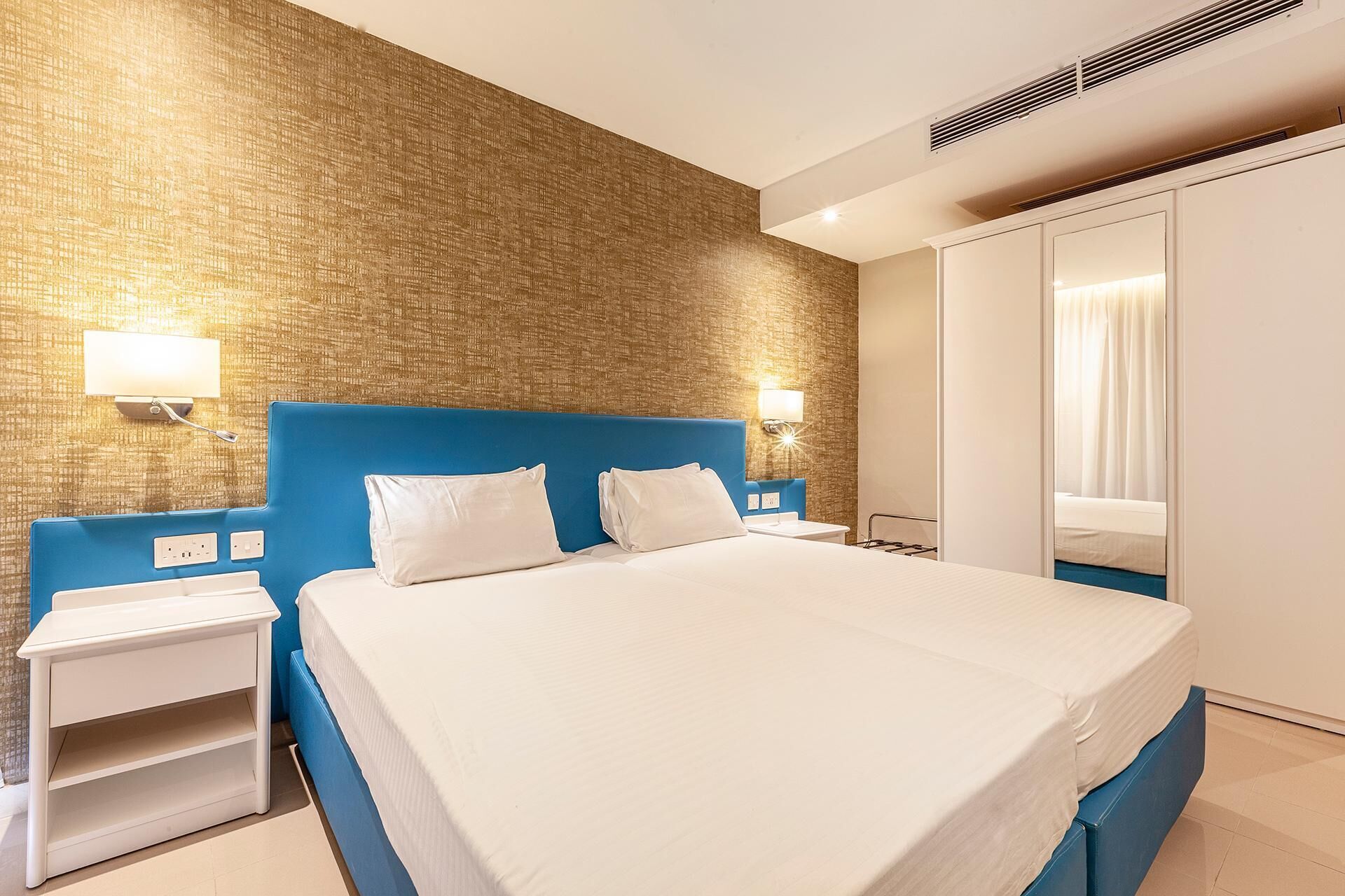 Habitación de hotel con una cama grande, una mesita de noche, un armario y una pared con textura.