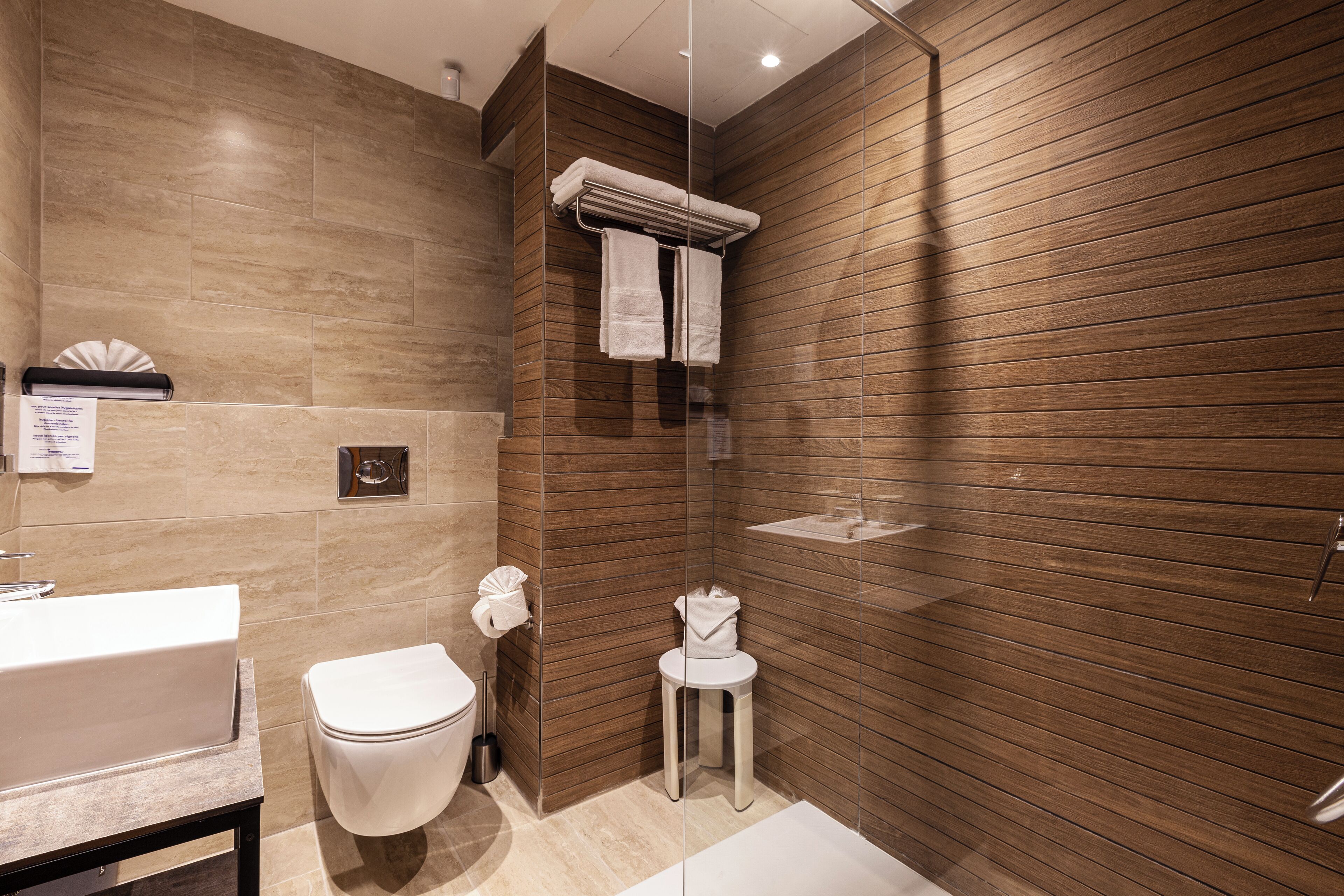 A modern bathroom with a wooden wall, a white toilet, a sink, and a glass shower enclosure.