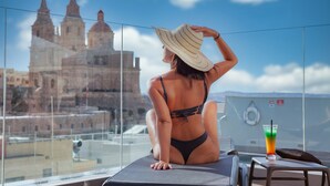 Une personne assise sur un balcon, d’où l’on peut admirer un bâtiment historique.