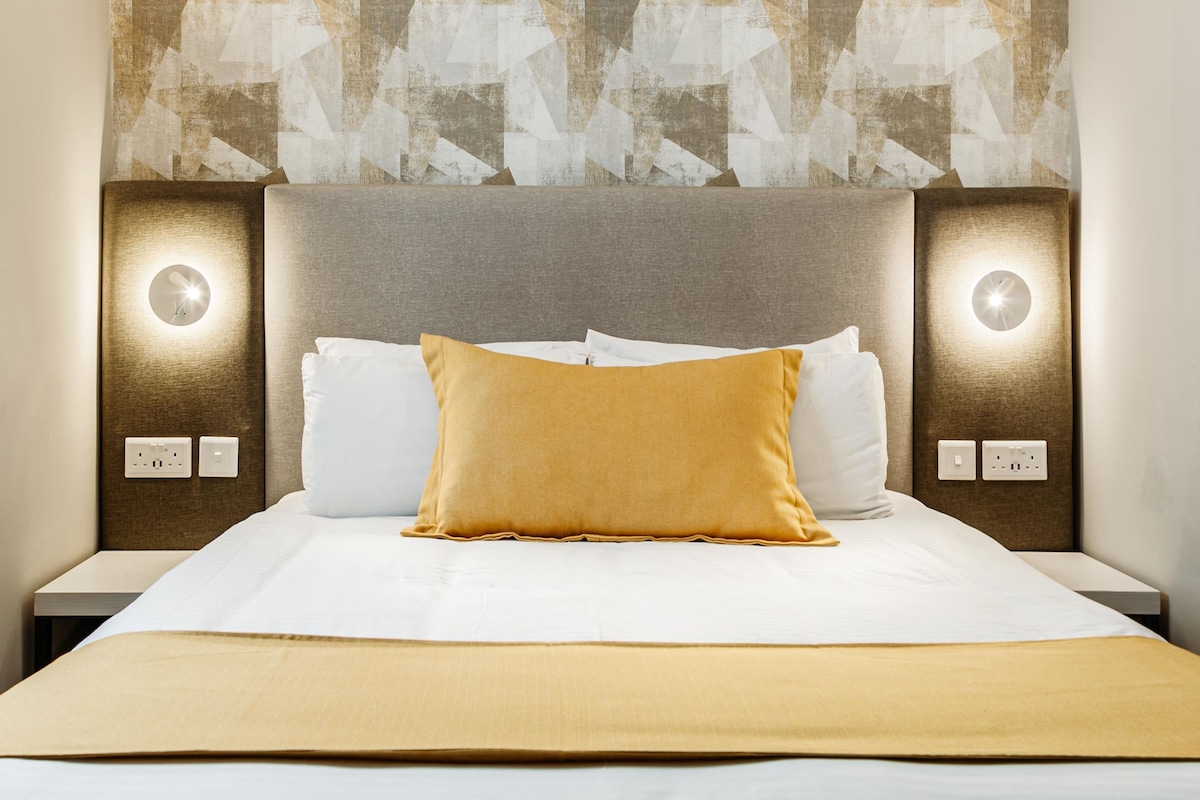 A hotel room with a large bed, two bedside tables, and a wall with geometric patterned wallpaper.
