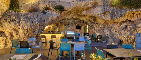 An outdoor dining area with stone walls, blue and white chairs, and tables.