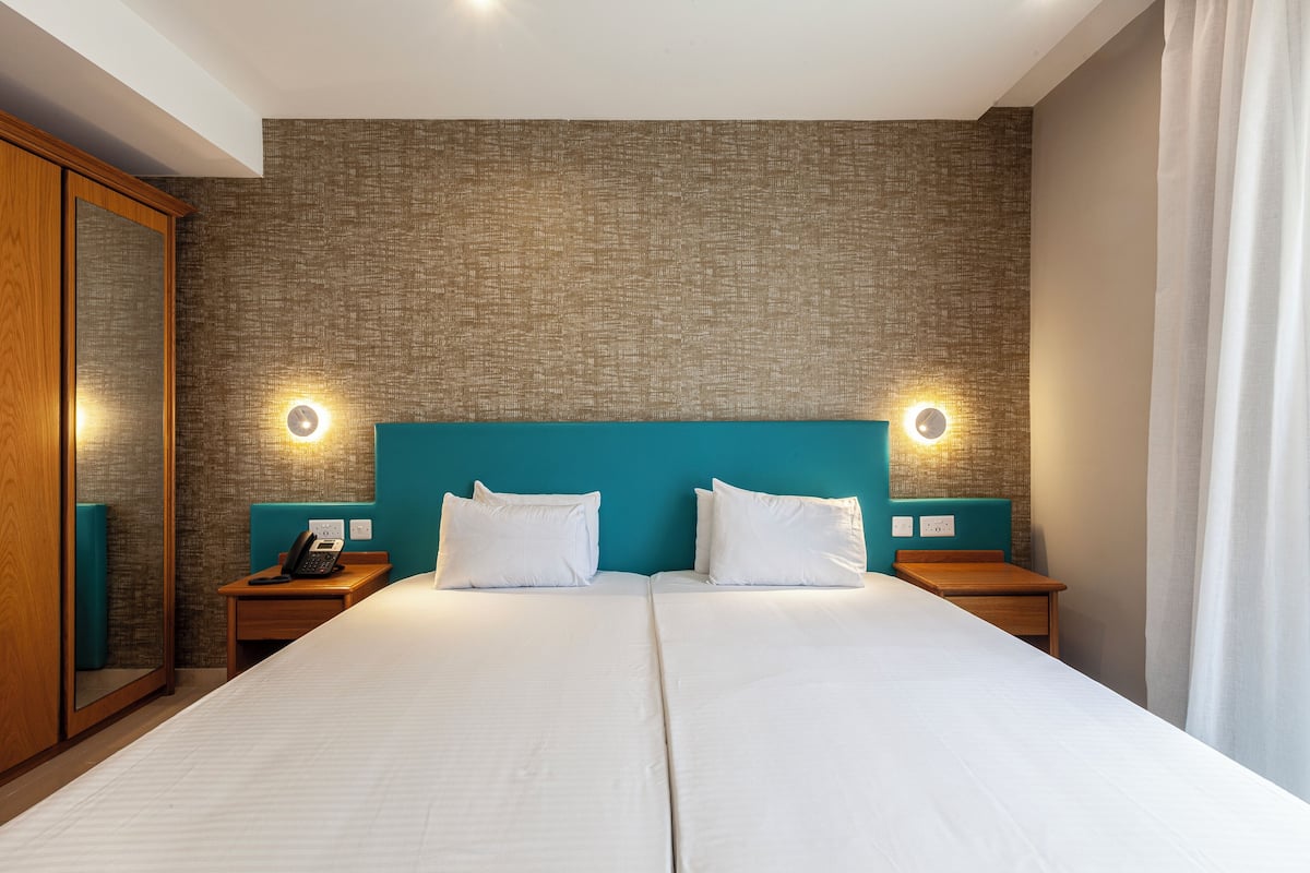 A double bed with white linens, two bedside tables with lamps, a wooden wardrobe, and a textured wall.