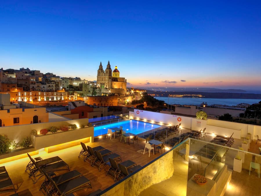 A rooftop pool area with lounge chairs and a view of a historic building and the sea.