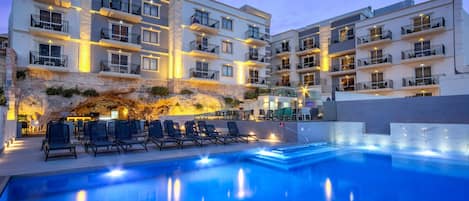 A multi-story hotel with a swimming pool, outdoor seating, and a rocky landscape.