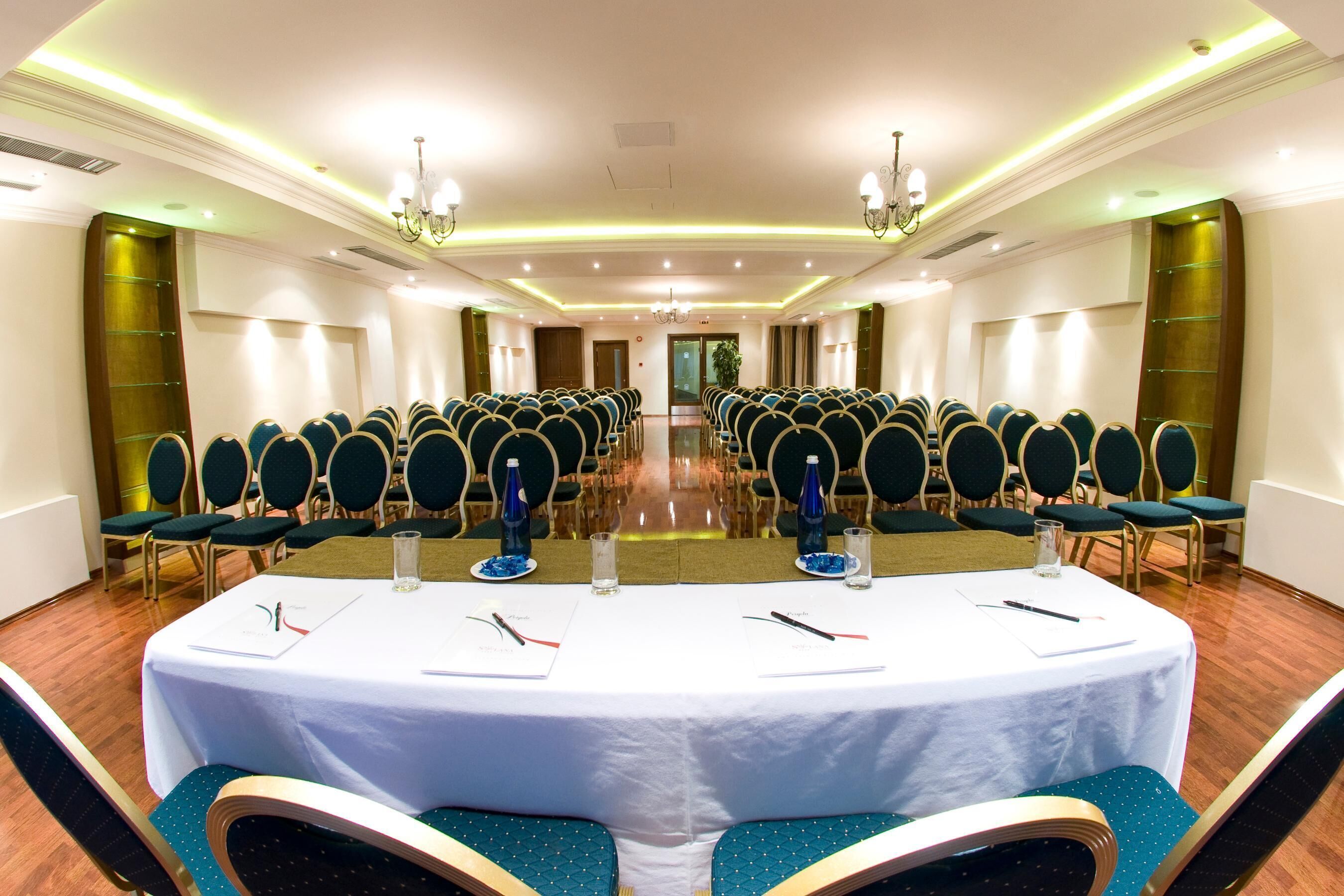 A conference room with rows of chairs, a long table with nameplates, and a chandelier.