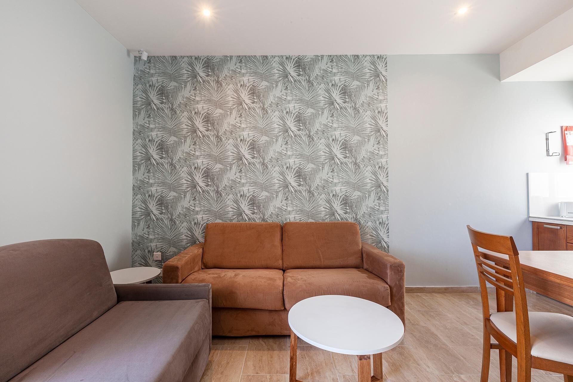 Un salon avec un canapé marron, une table ronde blanche et une chaise en bois.