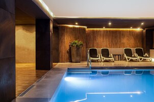 Un área de piscina interior moderna con pared de madera, una planta en maceta y sillones de descanso.