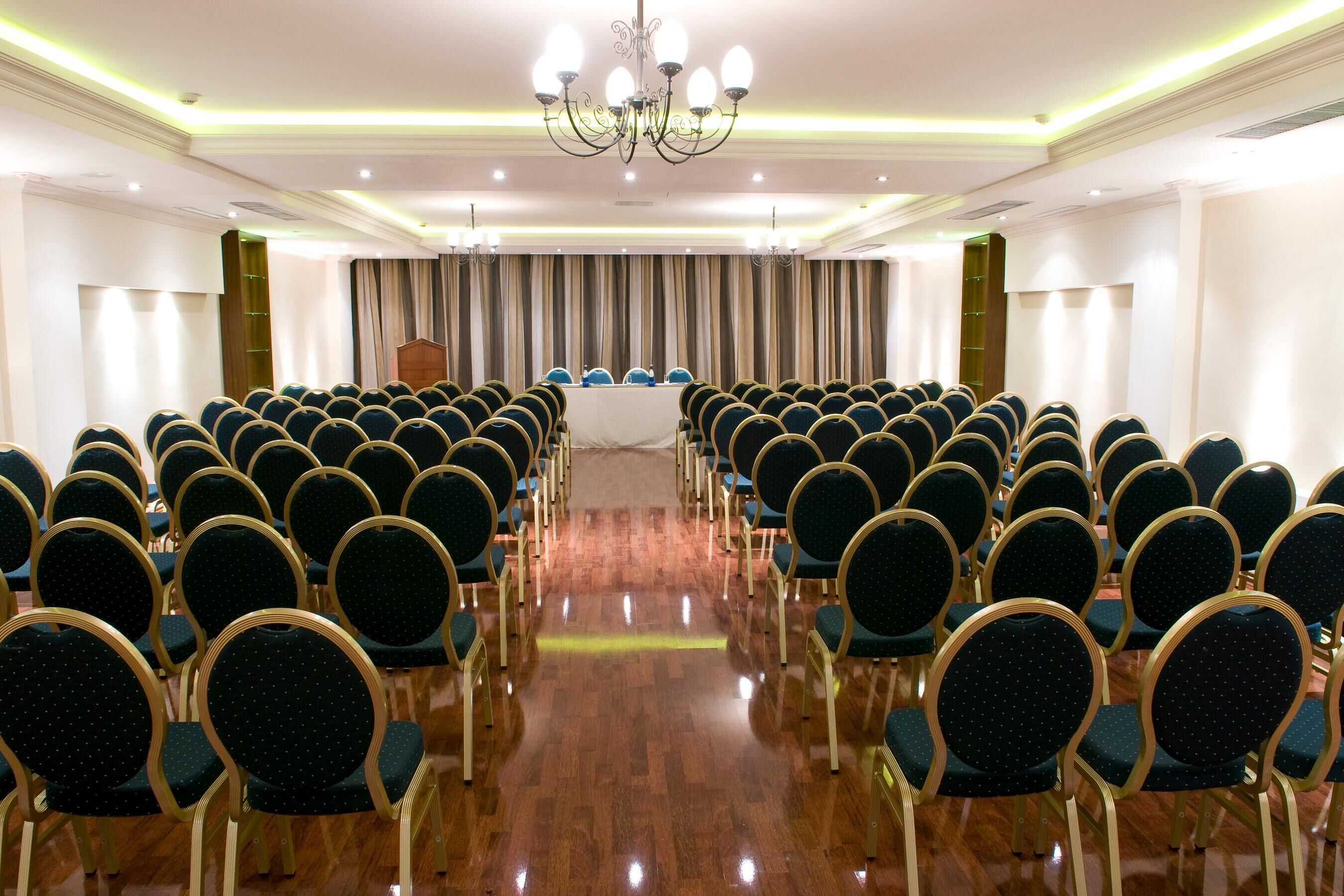 Ein Konferenzraum mit Stuhlreihen, die auf eine Bühne zeigen, einer Kristallleuchtre und einem hölzernen Rednerpult.