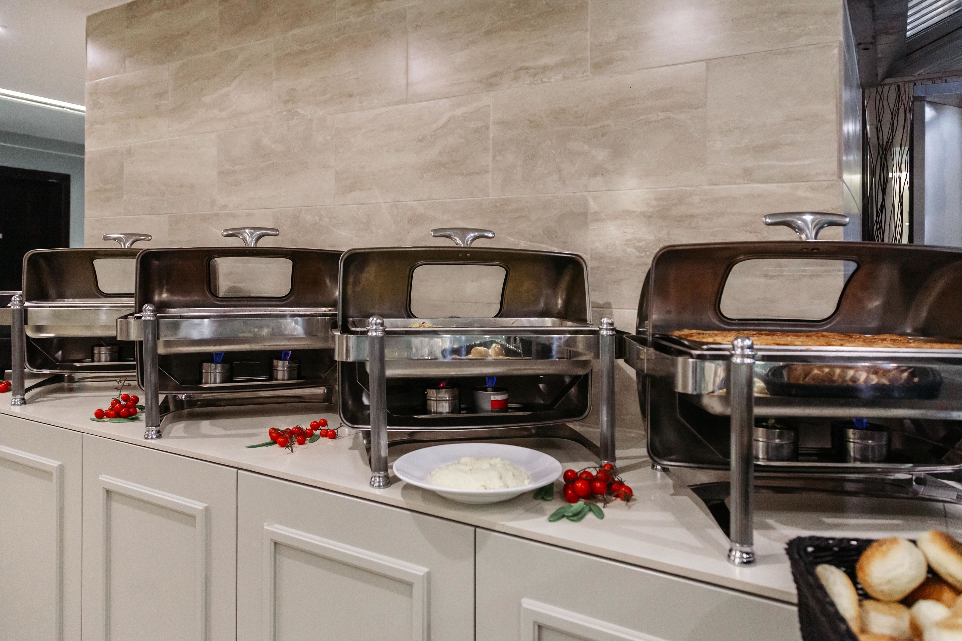 A buffet setup with multiple serving stations, a white plate with a white substance, and a basket of bread rolls.