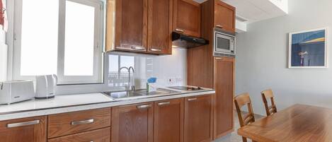 Una cocina moderna con armarios de madera, un lavamanos de acero inoxidable y un microondas empotrado.