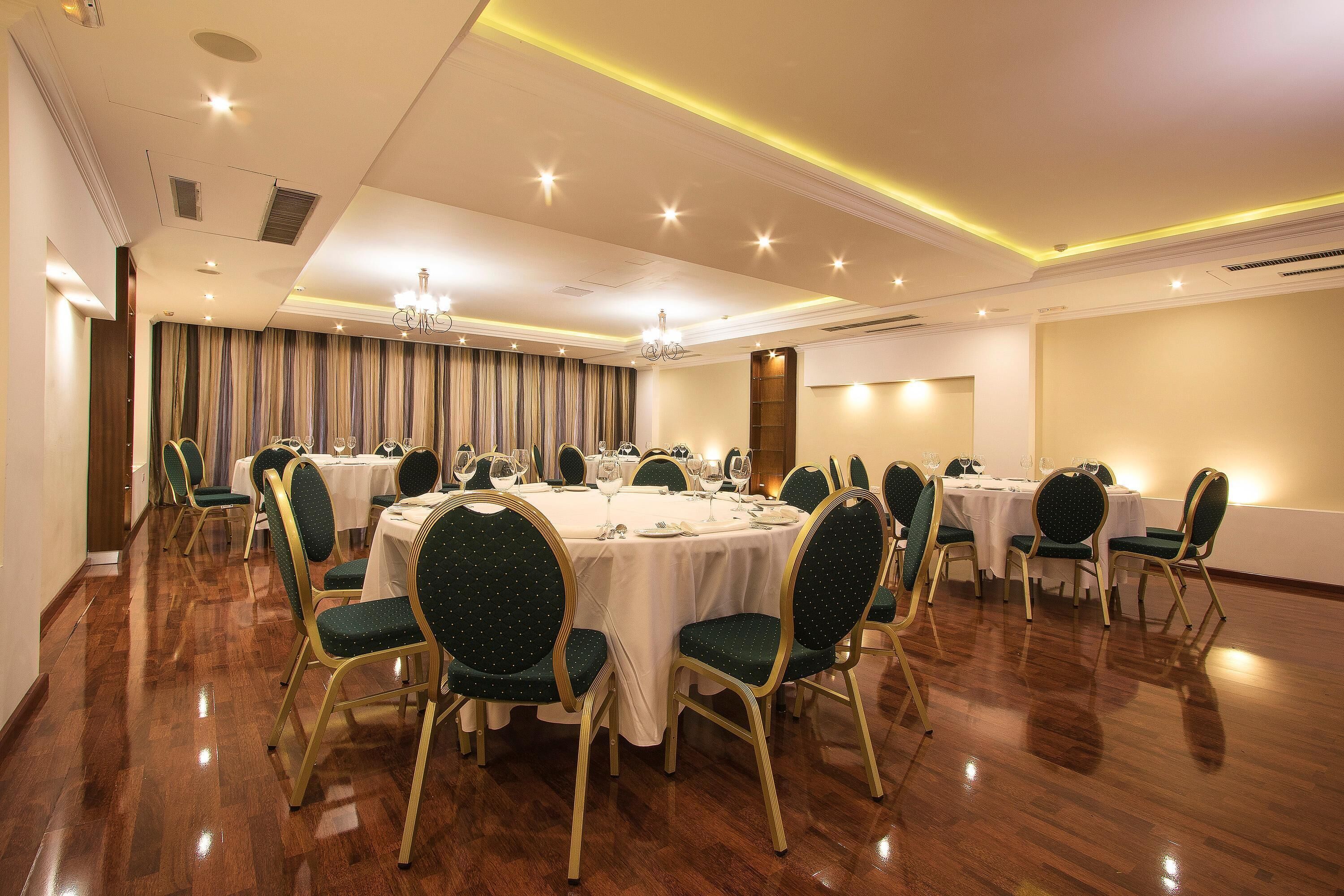 A banquet hall with round tables, green upholstered chairs, and chandeliers.