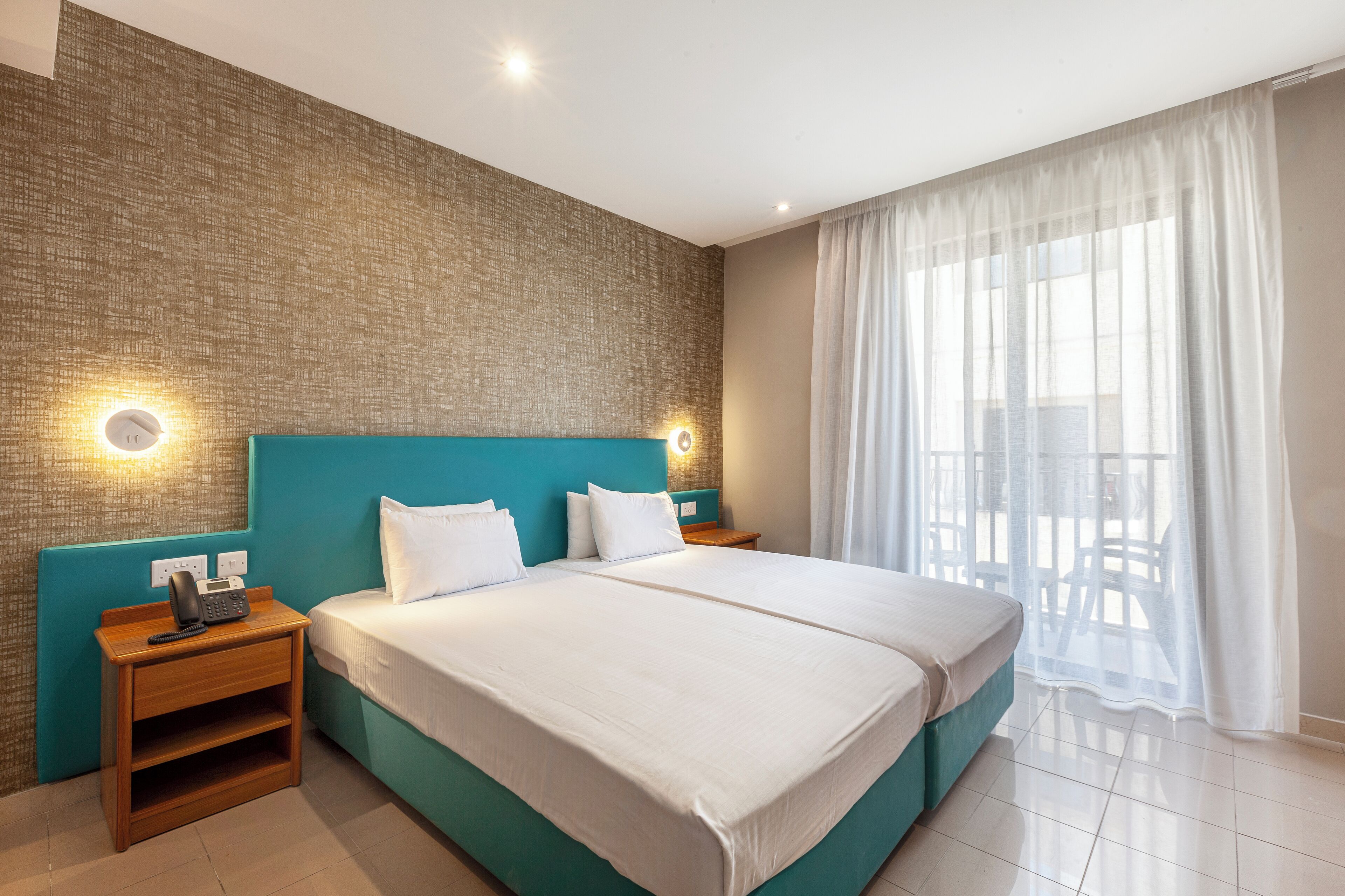 Una moderna camera d'albergo con un grande letto, un comodino in legno con un telefono e un lampadario a parete.