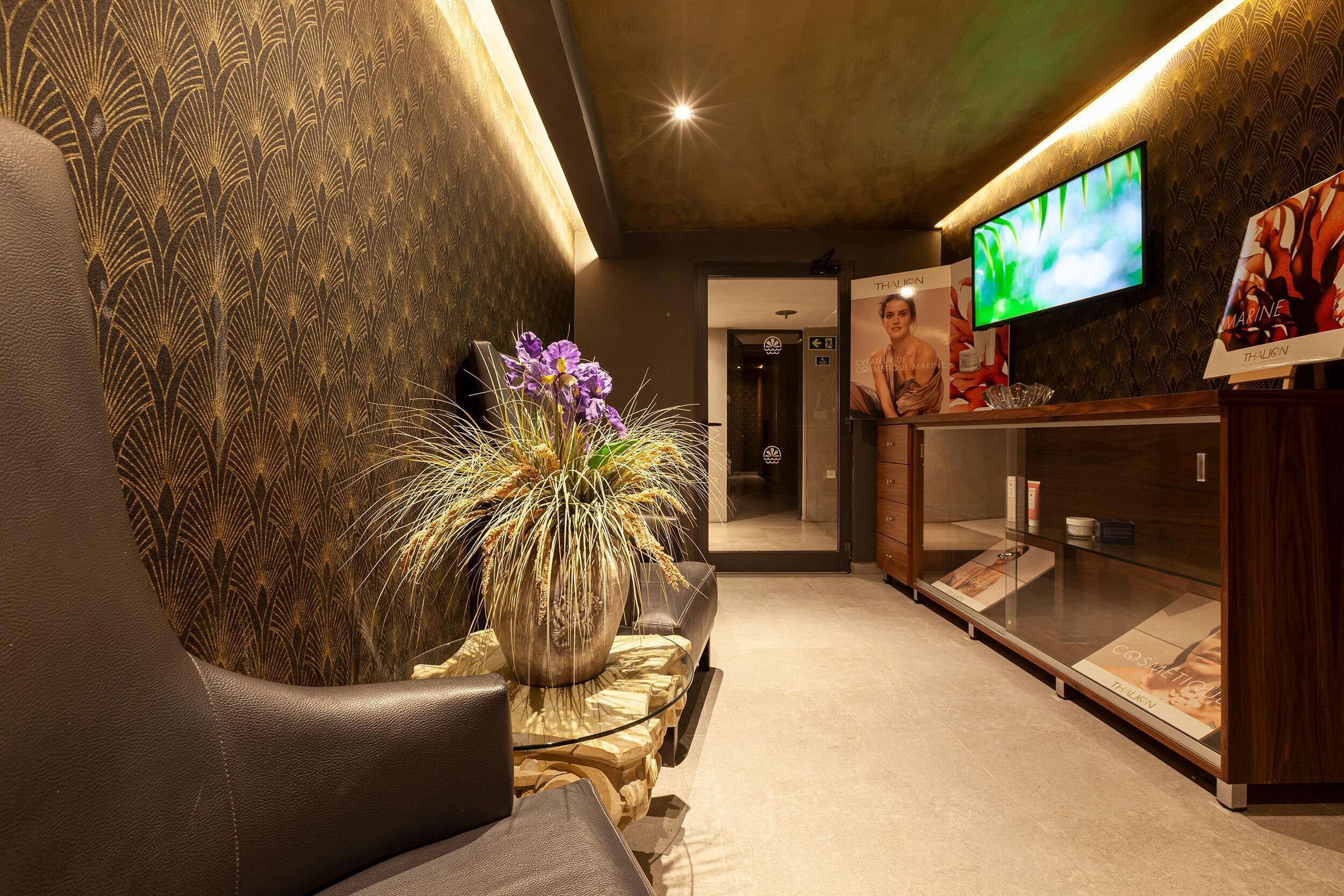 Eine moderne Lobby mit einer Couch, einer großen Kübelpflanze, einer Glasvitrine und einem an der Wand montierten Fernseher.