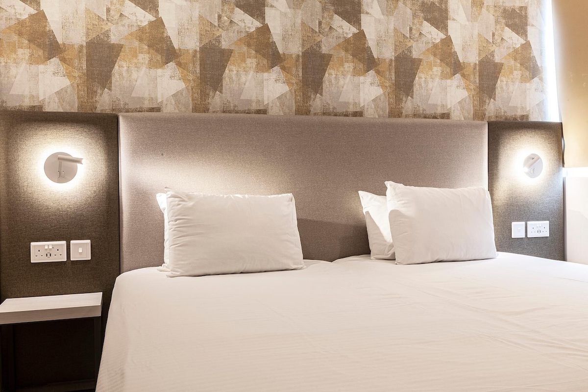 A hotel room with a modern design, featuring a geometric patterned wall, a neutral color palette, and a clean, minimalist aesthetic.
