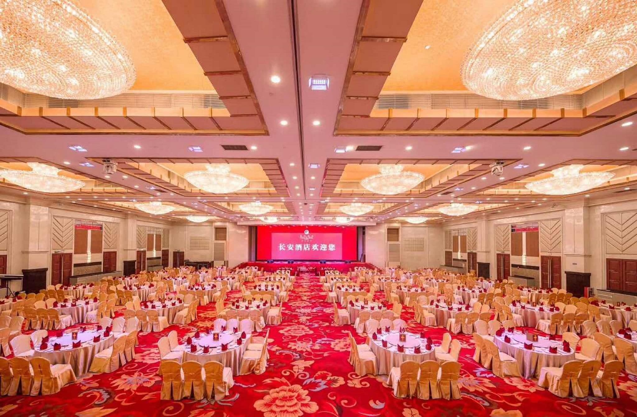 A banquet hall with round tables, chairs, and a stage with a red backdrop.