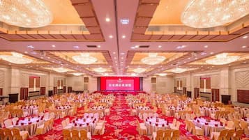 A banquet hall with round tables, chairs, and a stage with a red backdrop.