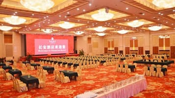 A large conference room with rows of tables and chairs, a stage with a screen, and chandeliers.