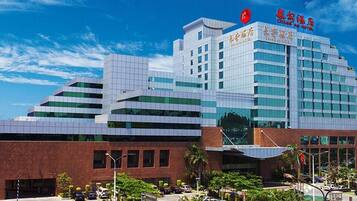 A modern hotel with a prominent red logo, multiple floors, and a parking area with trees.
