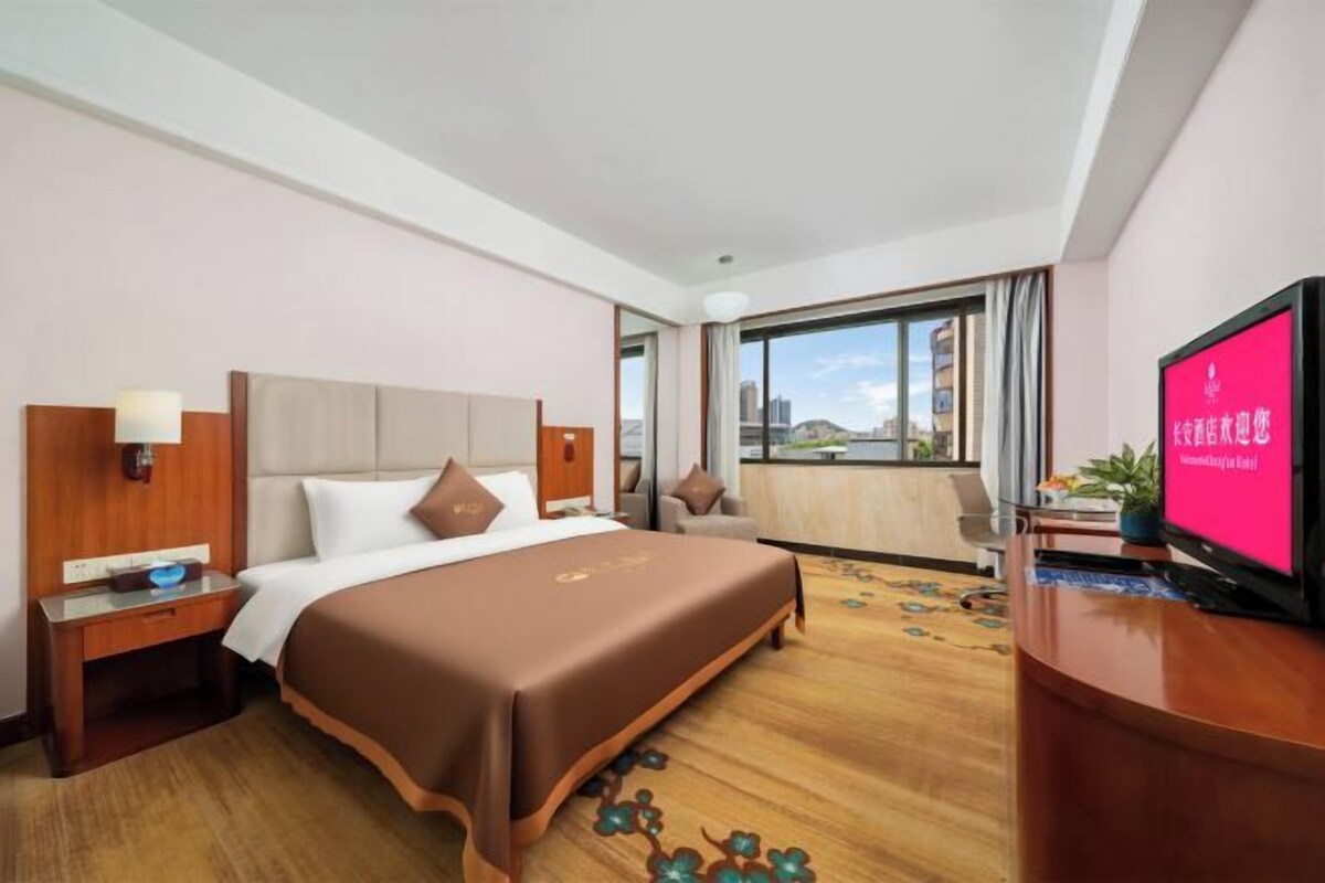A hotel room with a bed, a television, a desk, and a window with a view.