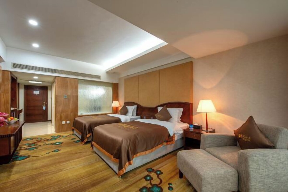 A hotel room with two beds, a sofa, a desk, and a patterned carpet.