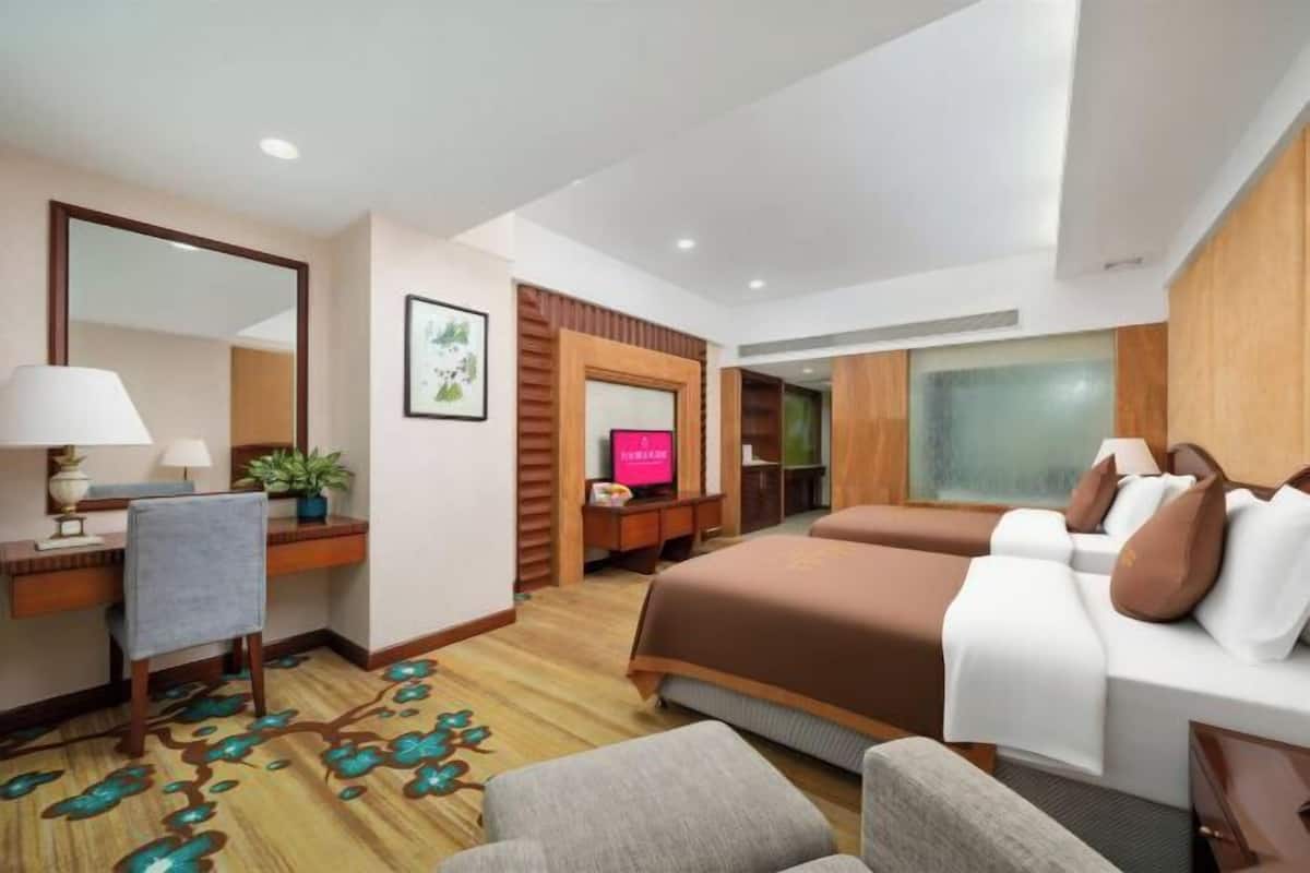 A hotel room with a bed, a desk with a lamp, a chair, a television, and a plant.