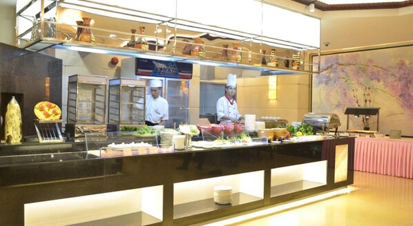 Área de buffet com diversas opções de comida e um chef preparando refeições.