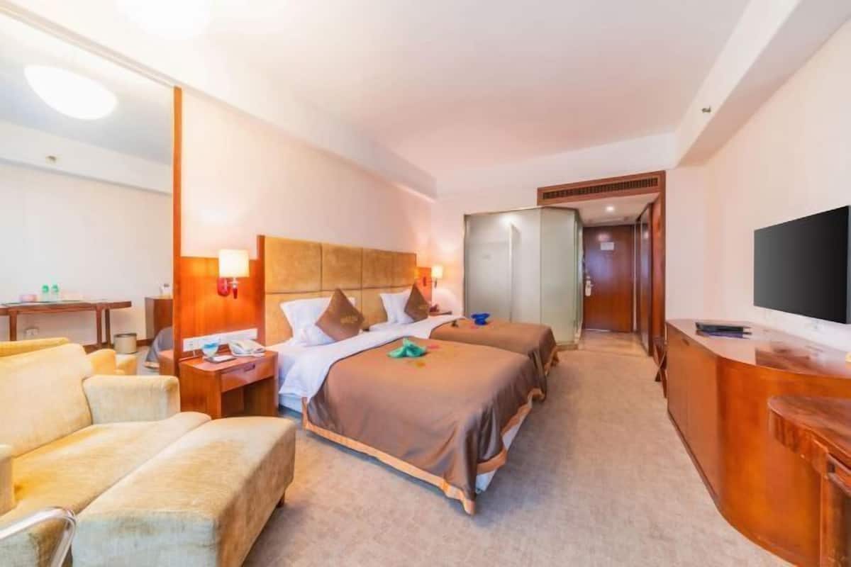 A hotel room with two beds, a desk, a TV, and a reception area.
