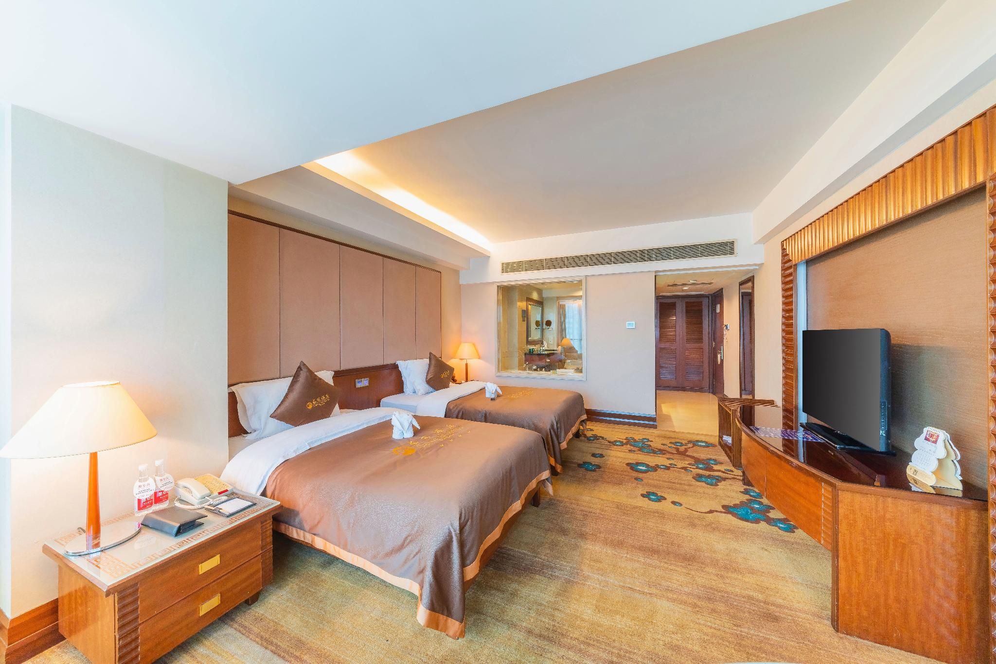 Een hotelkamer met twee bedden, een televisie, een bureau en een spiegel.