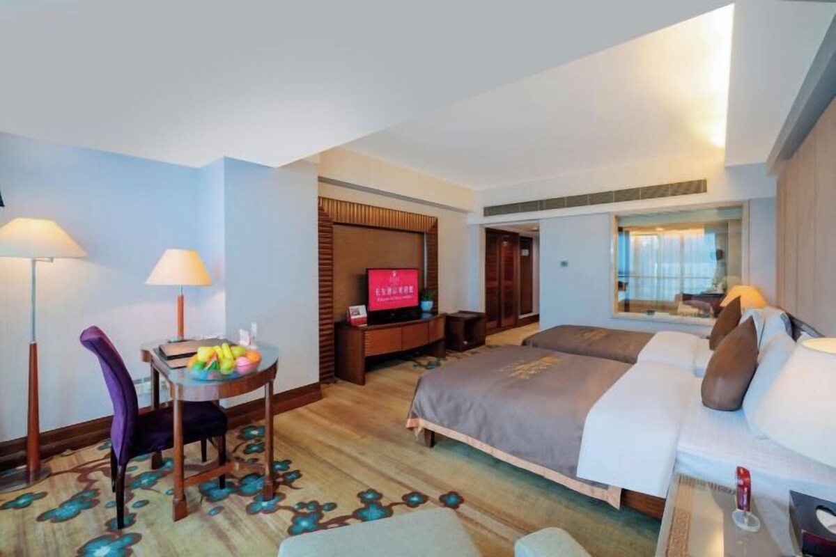 A hotel room with a bed, a desk with a chair, a TV, and a window.