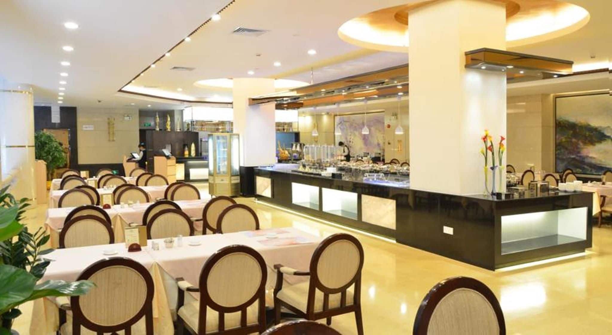 A restaurant with multiple dining tables, chairs, a central bar area, and a view of the kitchen in the background.