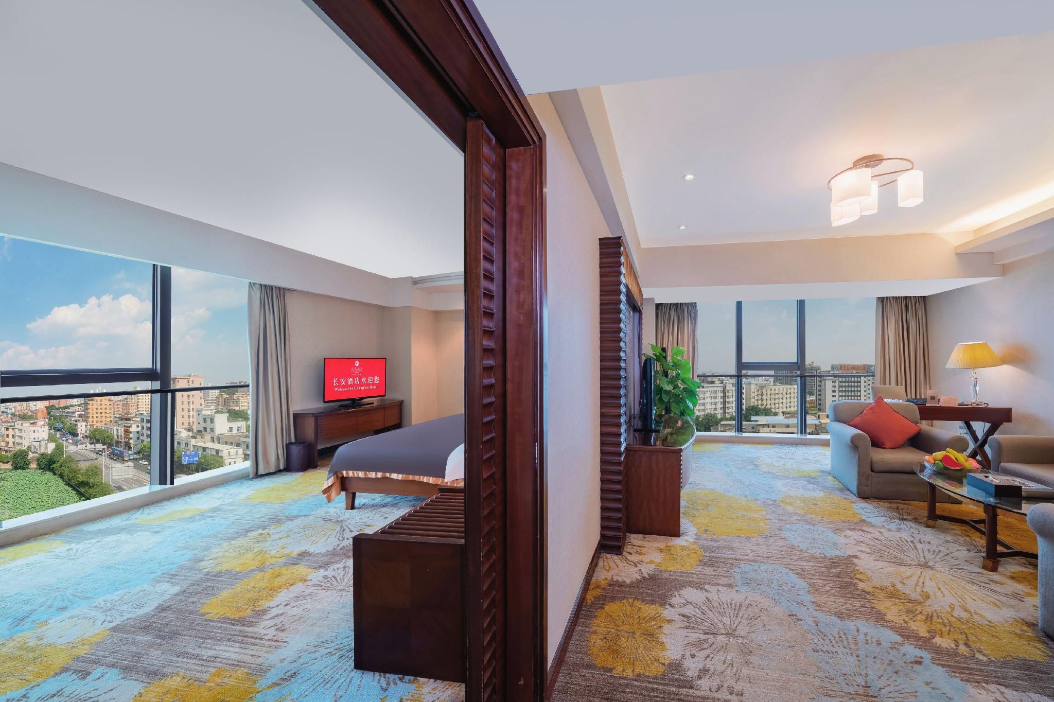 Habitación de hotel con cama, sofá, televisión y un amplio ventanal con vistas a la ciudad.