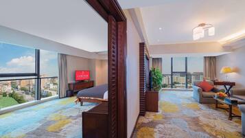 Habitación de hotel con cama, sofá, televisión y un amplio ventanal con vistas a la ciudad.