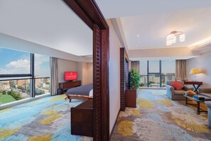Habitación de hotel con cama, sofá, televisión y un amplio ventanal con vistas a la ciudad.