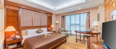 A hotel room with a large bed, a desk, a TV, and a view of the city.