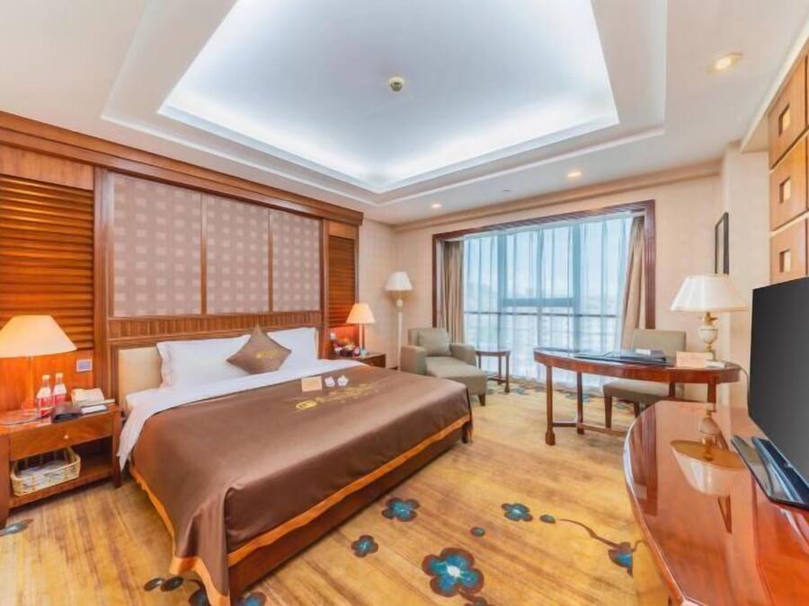 A hotel room with a large bed, a desk, a TV, and a view of the city.