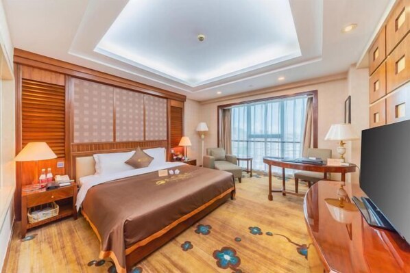 Habitación de hotel con una cama grande, un escritorio, un televisor y vistas a la ciudad.