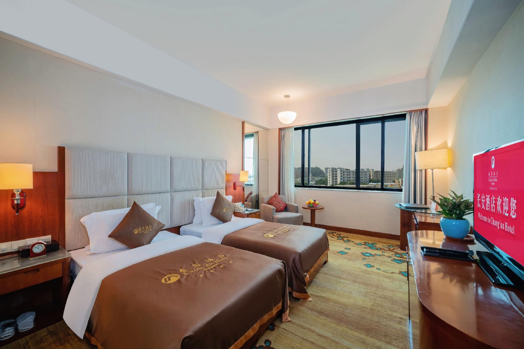 Habitación de hotel con dos camas, un escritorio, un televisor y ventana con vista a la ciudad.