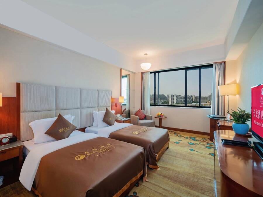 Habitación de hotel con dos camas, un escritorio, un televisor y ventana con vista a la ciudad.