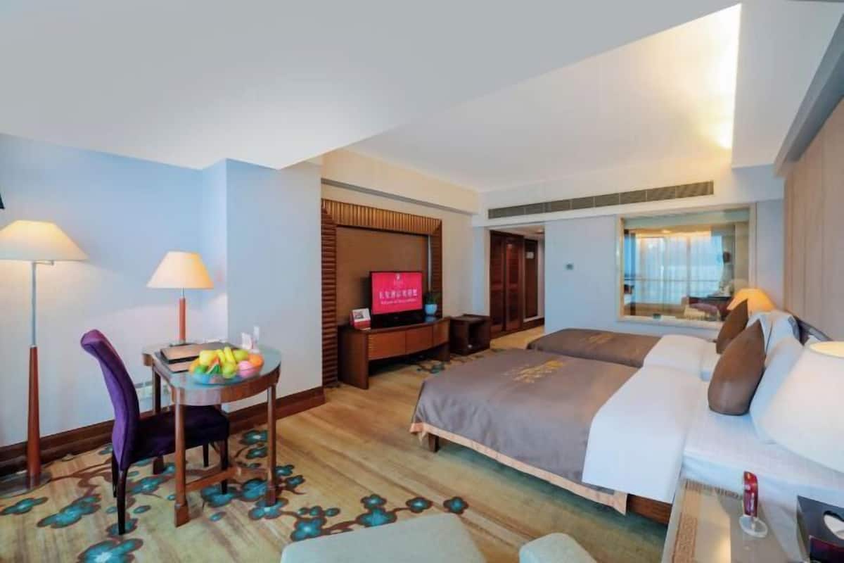 A hotel room with a bed, a desk with a chair, a TV, and a window.