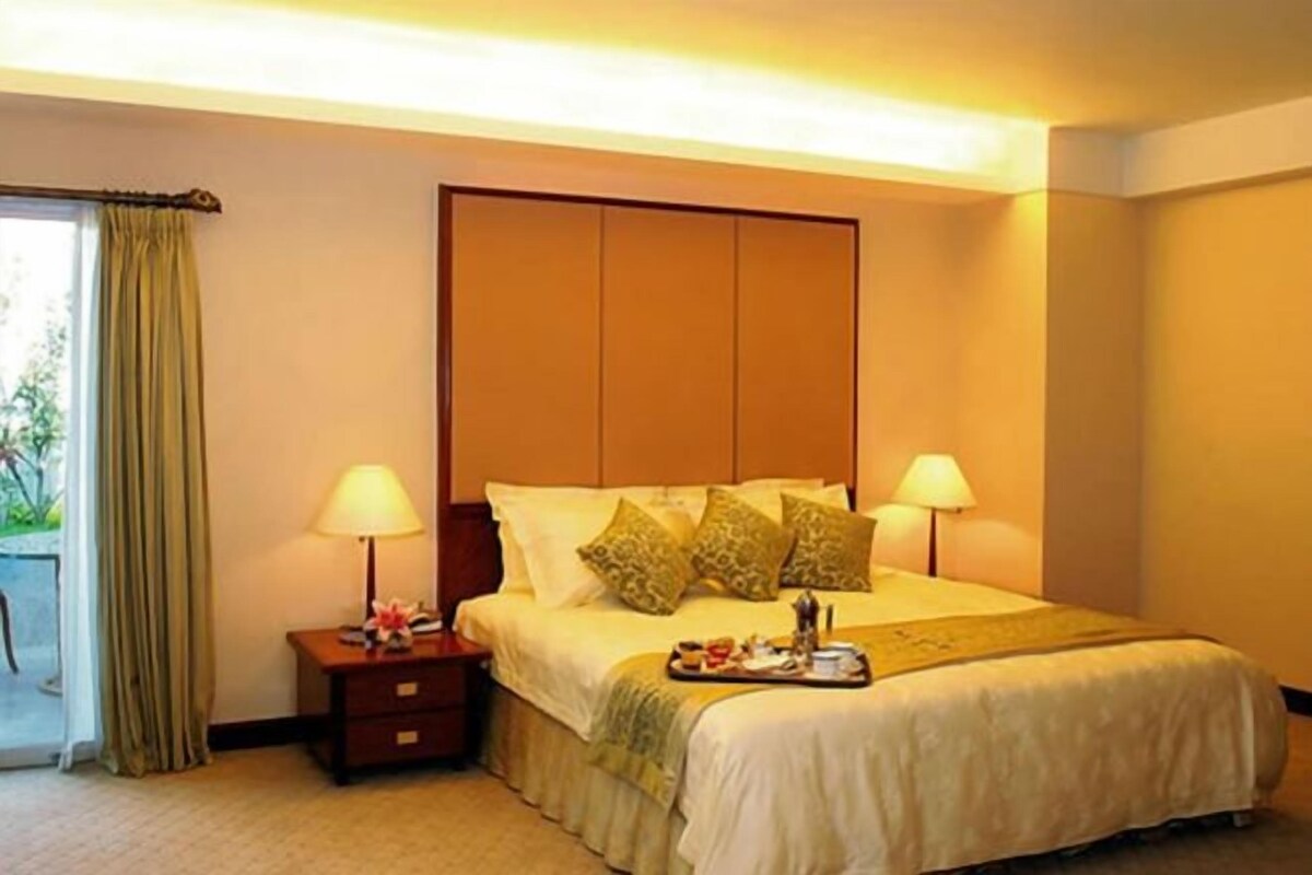 A hotel room with a bed, two bedside lamps, a tray with breakfast items, a nightstand, and a window with curtains.