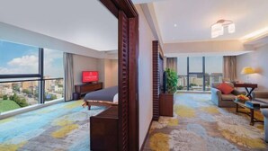 Una habitación de hotel moderna con un ventanal grande, una cama, un sofá, un televisor y una planta.