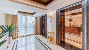 Un vestíbulo de hotel con suelo de mármol, mostrador de recepción, un amplio ventanal y una planta.