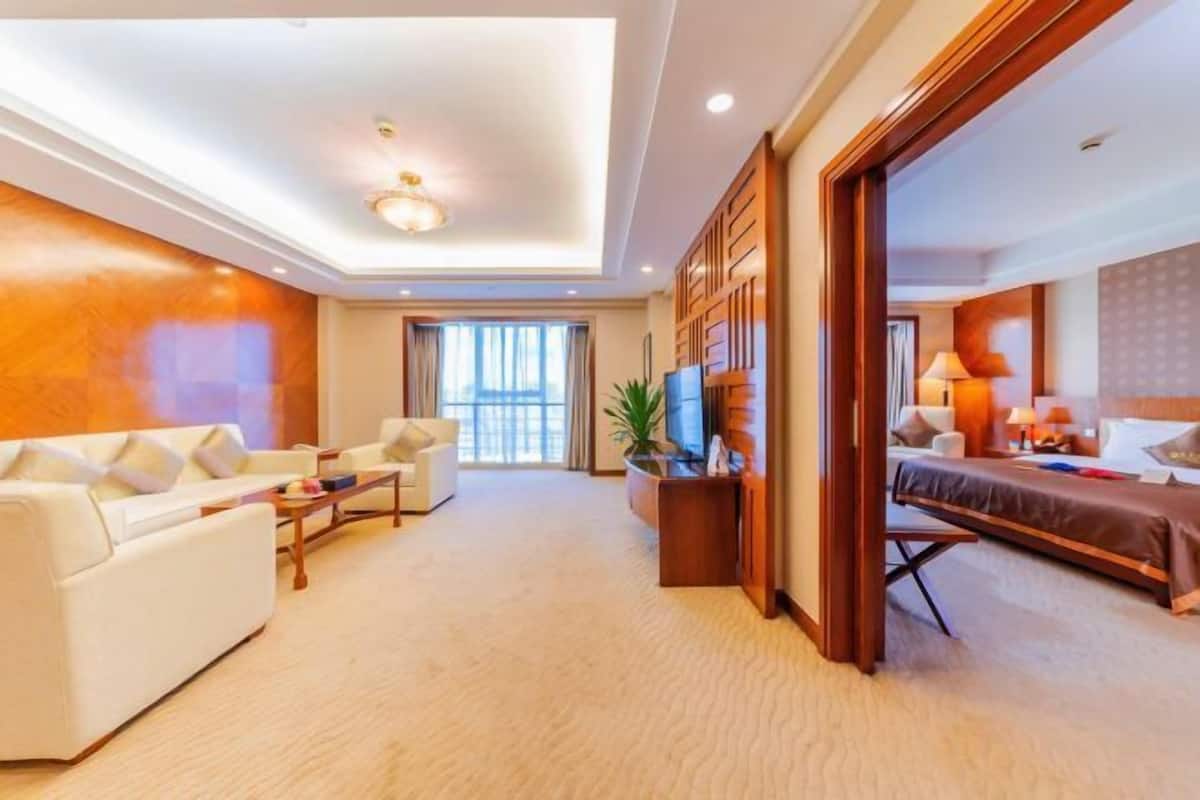 A hotel room with a sofa, a bed, a TV, and a lamp.