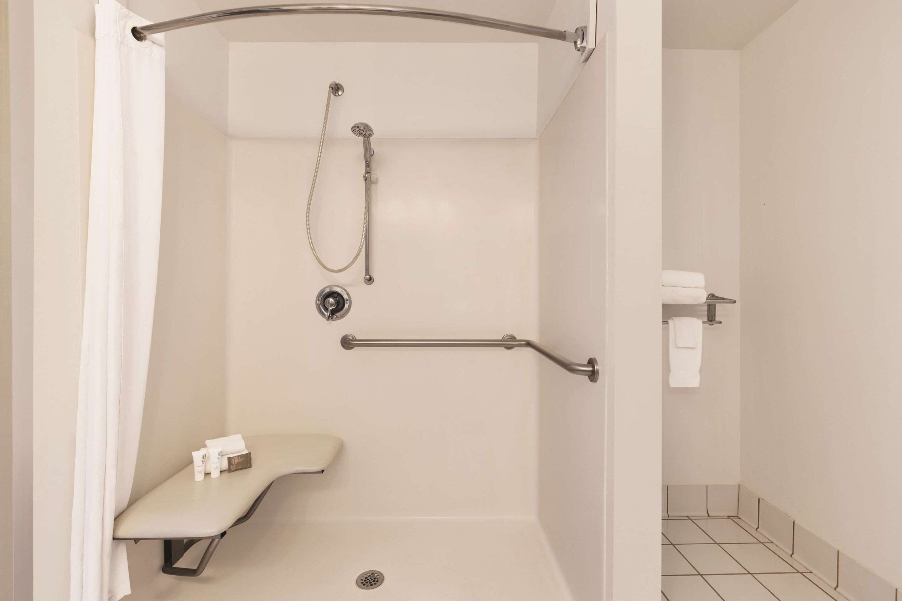 A shower area with a grab bar, a bench, and a towel rack.