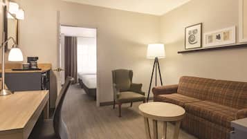 Una habitación de hotel con cama, escritorio con lámpara, silla, sofá y una mesita.